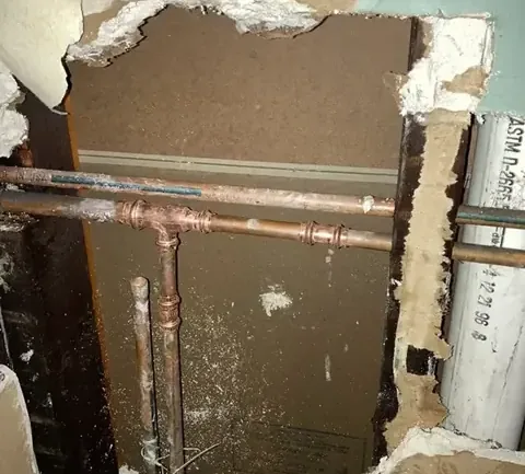 Section of wall opened up to reach leaking copper supply pipes